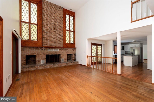 unfurnished living room with visible vents, a brick fireplace, a high ceiling, and hardwood / wood-style flooring