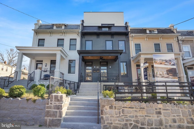 townhome / multi-family property with a porch, brick siding, mansard roof, and stairs