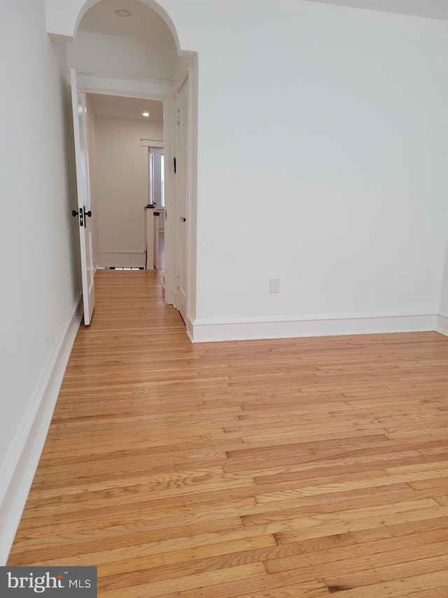 unfurnished room featuring arched walkways, light wood-style floors, and baseboards