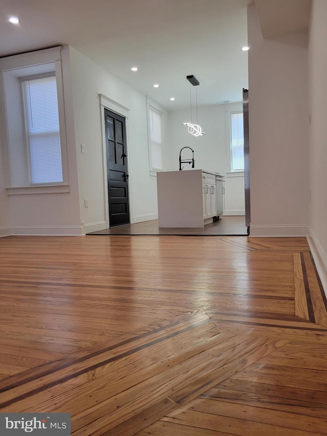unfurnished living room with parquet flooring, a sink, baseboards, and recessed lighting