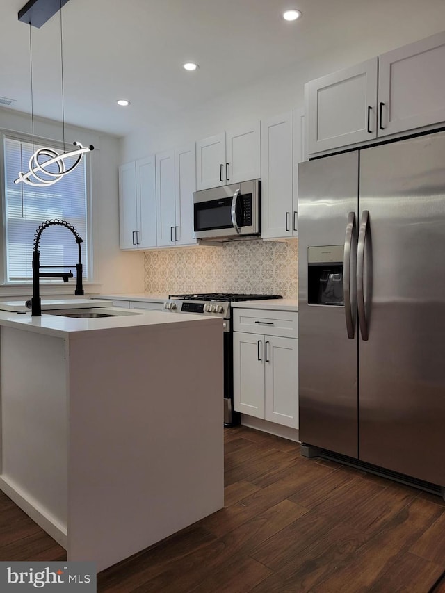 kitchen with tasteful backsplash, appliances with stainless steel finishes, dark wood-style flooring, a sink, and hanging light fixtures