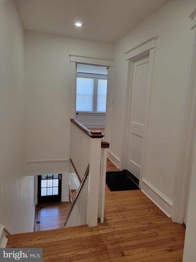 hall featuring wood finished floors, an upstairs landing, and recessed lighting