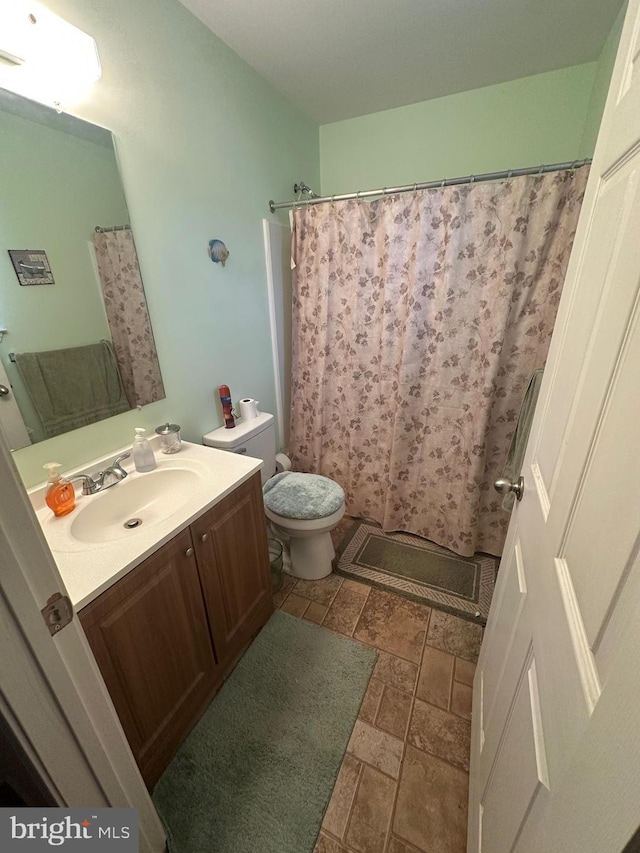 full bathroom with stone tile flooring, toilet, vanity, and curtained shower