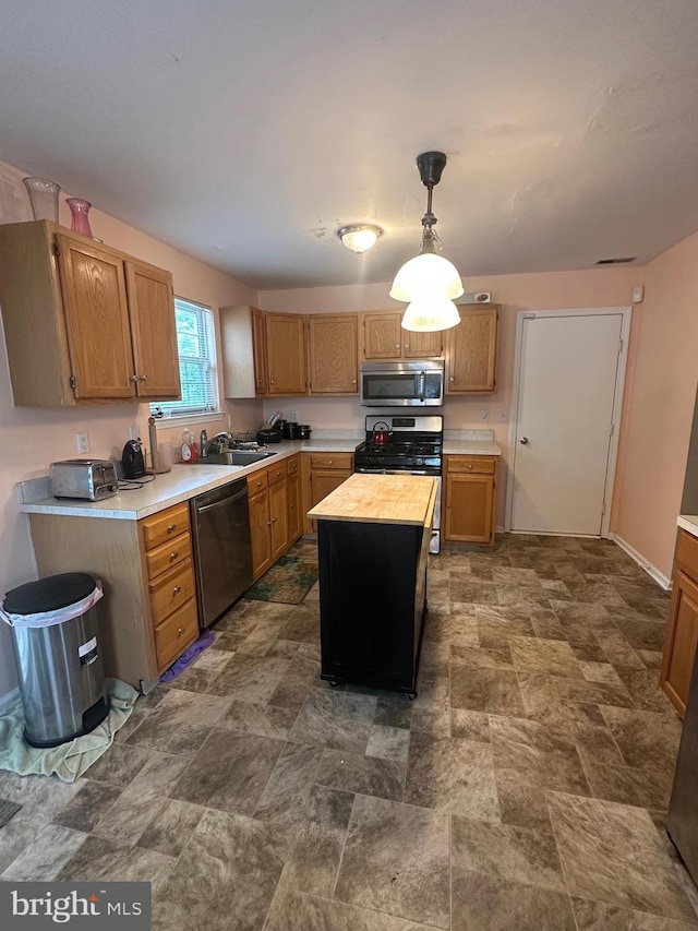 kitchen with stainless steel appliances, a sink, stone finish floors, decorative light fixtures, and a center island