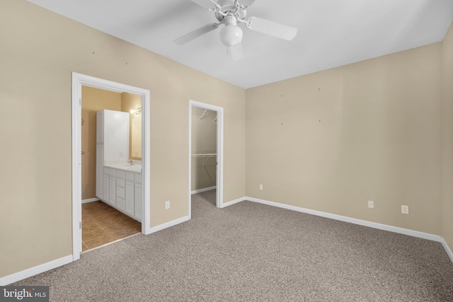 unfurnished bedroom with carpet flooring, a sink, a walk in closet, baseboards, and a closet