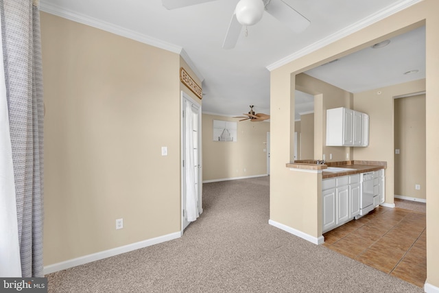 kitchen with crown molding, baseboards, light colored carpet, white cabinetry, and a ceiling fan