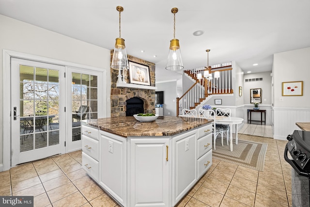 kitchen with range, light tile patterned floors, white cabinetry, dark stone countertops, and wainscoting
