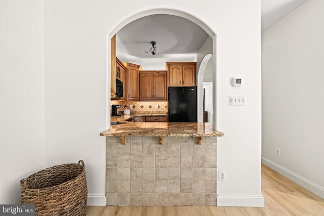 kitchen featuring tasteful backsplash, arched walkways, light wood-type flooring, black appliances, and light stone counters
