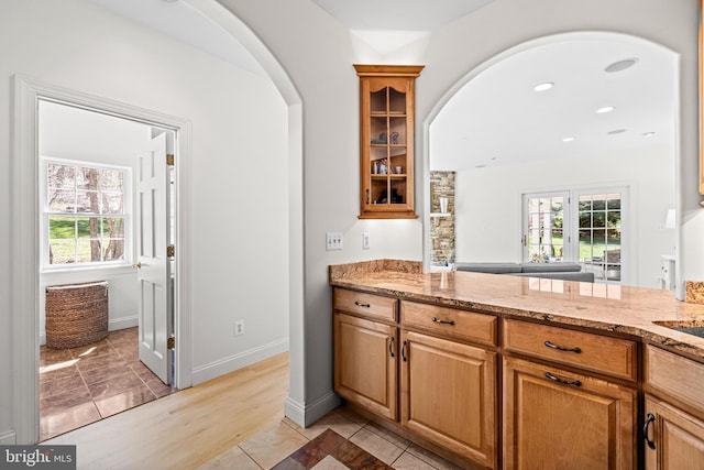 kitchen with arched walkways, glass insert cabinets, and plenty of natural light