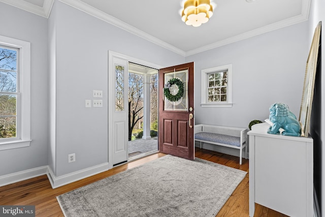 foyer entrance with a chandelier, crown molding, wood finished floors, and baseboards