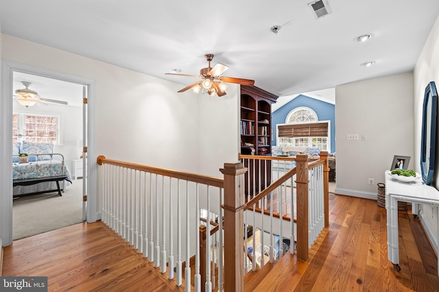 corridor featuring wood finished floors, visible vents, an upstairs landing, and a wealth of natural light