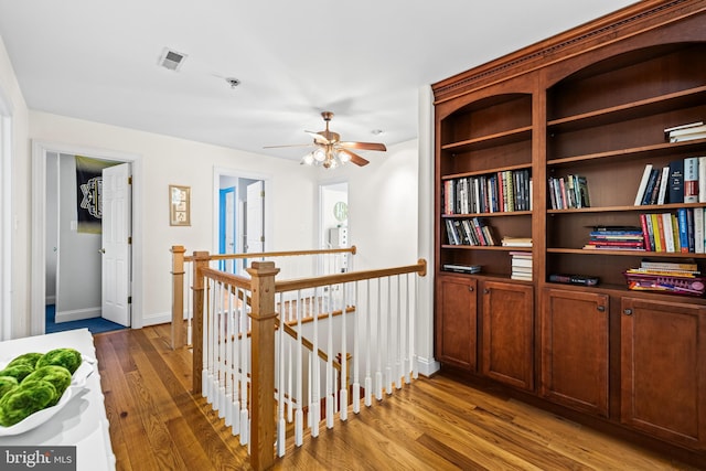 hall with wood finished floors, visible vents, baseboards, and an upstairs landing