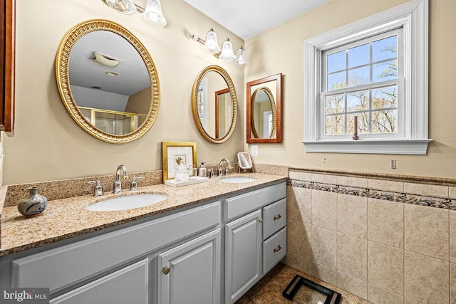 full bath with double vanity, tile walls, a sink, and a wainscoted wall