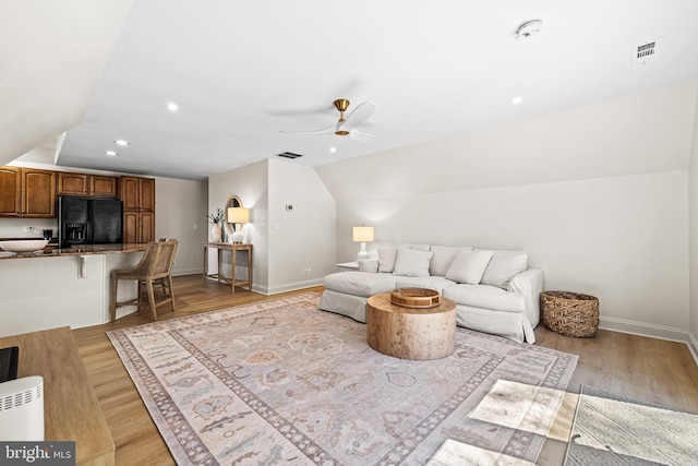 living area featuring visible vents, baseboards, light wood finished floors, and vaulted ceiling