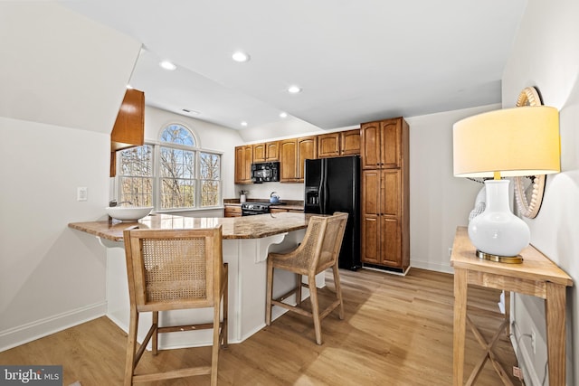 kitchen featuring a peninsula, light wood-type flooring, black appliances, and brown cabinets