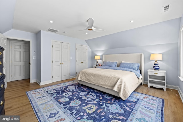 bedroom featuring light wood-style floors, visible vents, multiple closets, and lofted ceiling