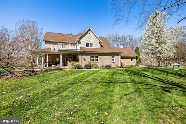 back of property with a balcony, a chimney, a patio area, brick siding, and a yard
