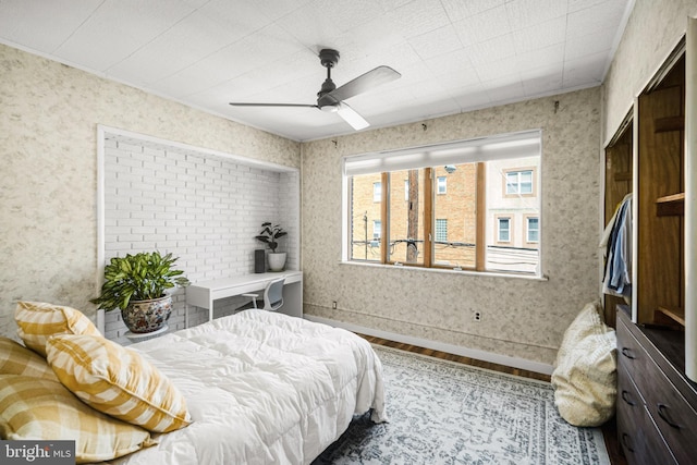 bedroom with wallpapered walls, wood finished floors, and a ceiling fan