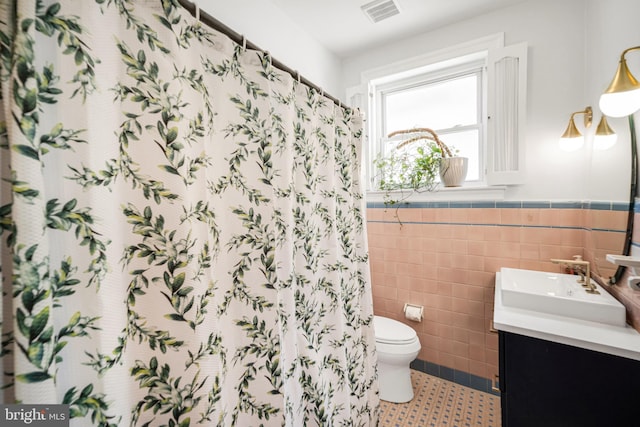 bathroom with visible vents, toilet, tile walls, vanity, and wainscoting