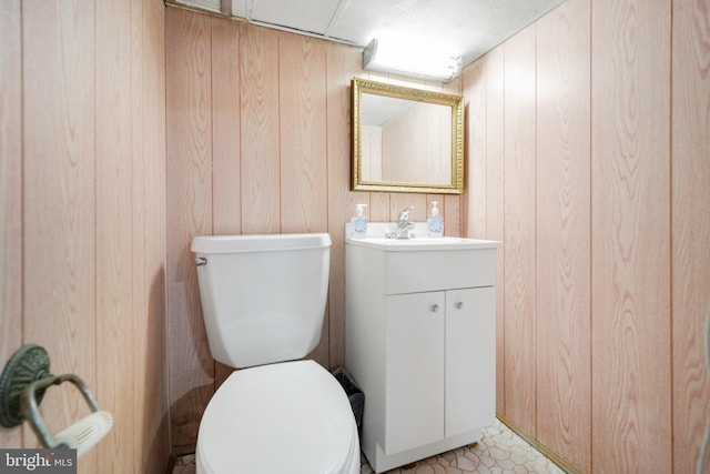 half bath with toilet, wood walls, and vanity