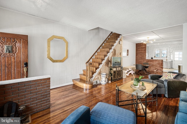 living room with brick wall, a chandelier, a textured ceiling, wood finished floors, and stairs
