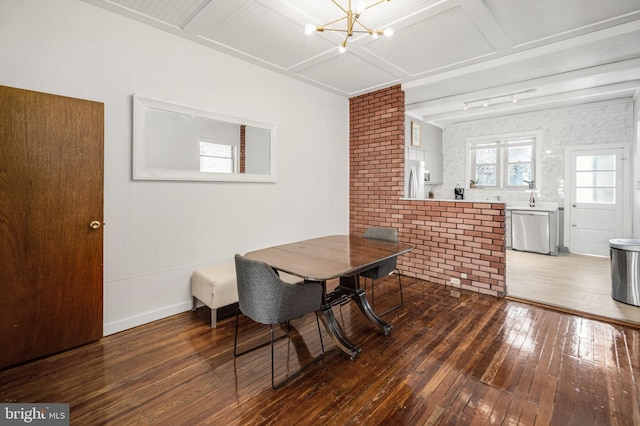 dining area featuring a chandelier, brick wall, baseboards, and hardwood / wood-style flooring