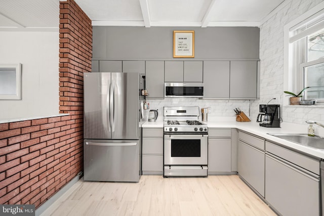 kitchen featuring a sink, gray cabinets, appliances with stainless steel finishes, and brick wall