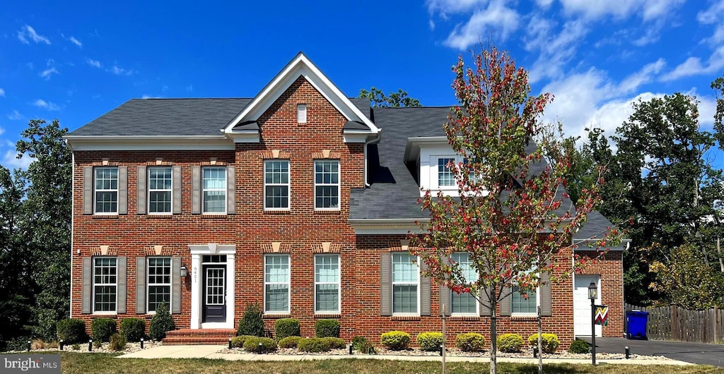 view of front facade with brick siding, a shingled roof, and fence