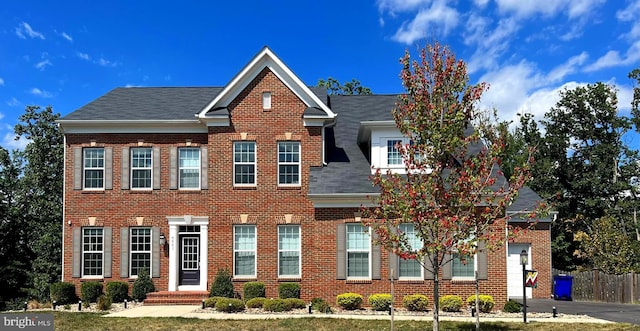 view of front facade with brick siding, a shingled roof, and fence
