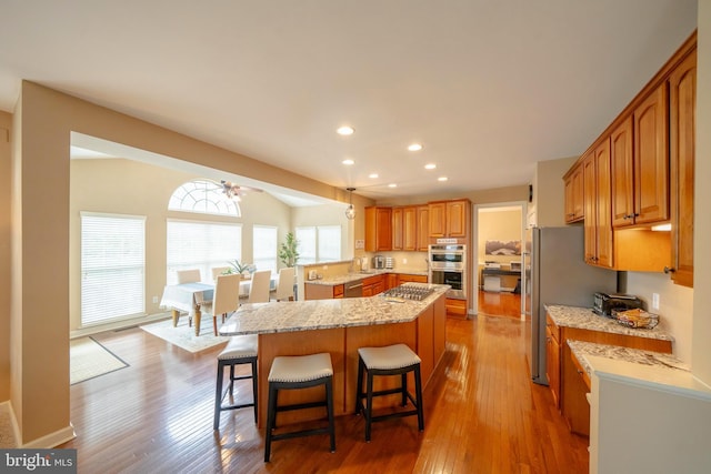869 Bourban Ln, West Grove, PA 19390 - kitchen featuring stainless steel appliances, a kitchen bar, wood finished floors, light stone counters, and brown cabinetry