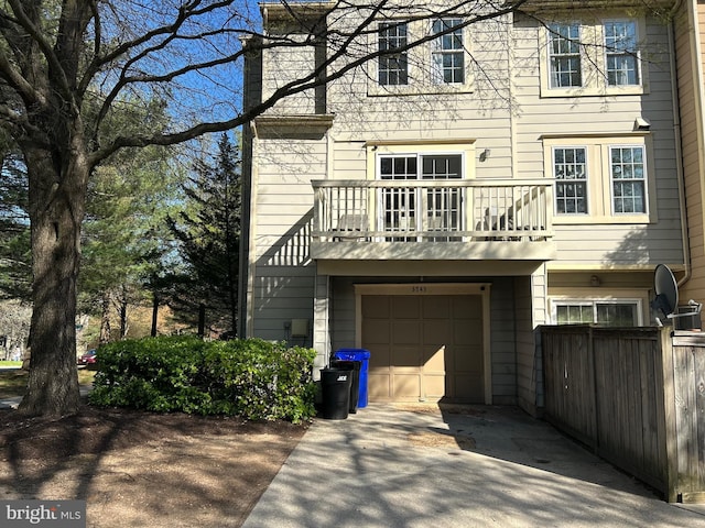 rear view of property featuring an attached garage, fence, a balcony, and concrete driveway