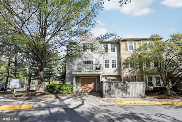 view of property with an attached garage, driveway, a balcony, and fence