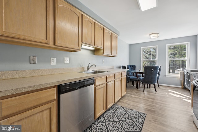 kitchen with stainless steel dishwasher, light countertops, a sink, and light wood-style flooring