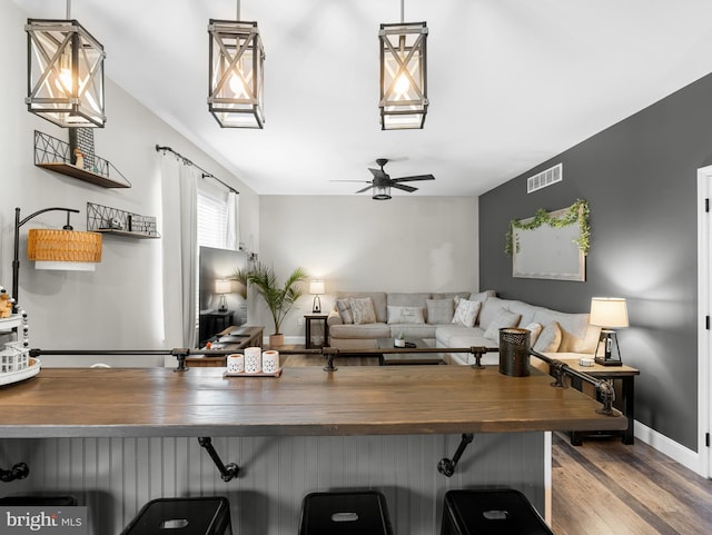 living room with visible vents, baseboards, wood finished floors, and ceiling fan