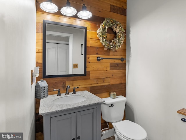 half bathroom with toilet, wood walls, and vanity