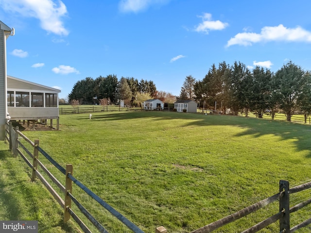 view of yard featuring a sunroom, fence, an outdoor structure, a storage unit, and a rural view