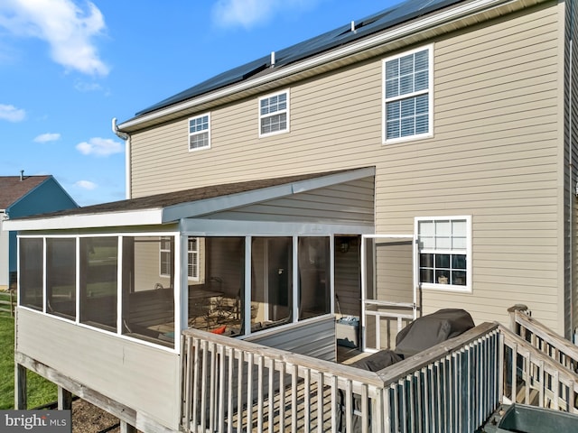 rear view of property featuring a sunroom and roof mounted solar panels