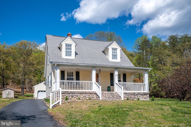 cape cod house featuring a front lawn, roof with shingles, a porch, and an outbuilding