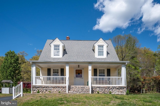 new england style home with roof with shingles, a porch, and a front yard