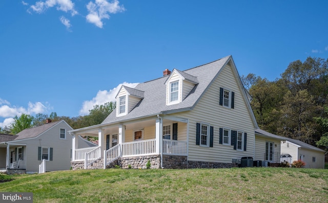 cape cod-style house with central AC unit, a chimney, a shingled roof, covered porch, and a front yard