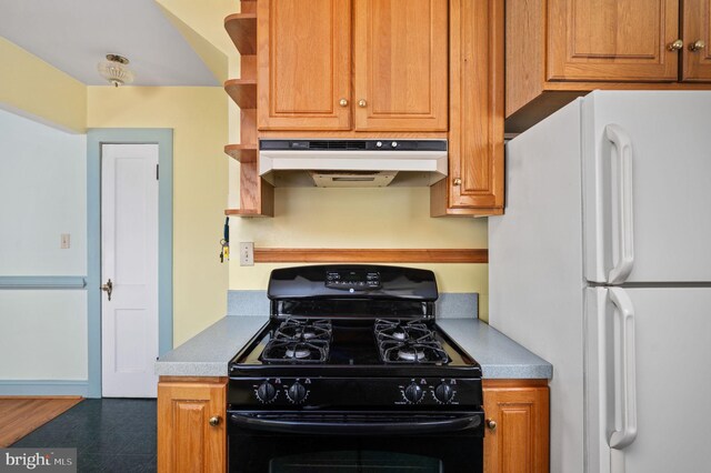 kitchen featuring brown cabinets, tile patterned floors, under cabinet range hood, freestanding refrigerator, and black gas stove