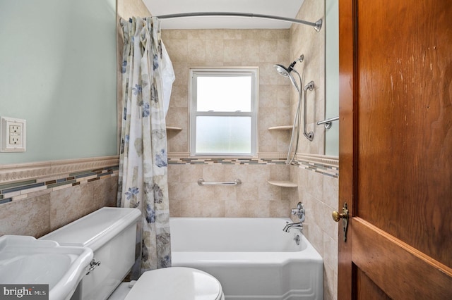bathroom with a sink, wainscoting, shower / bathtub combination with curtain, tile walls, and toilet