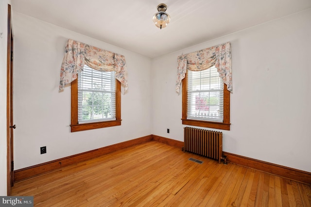 empty room with visible vents, wood-type flooring, baseboards, and radiator