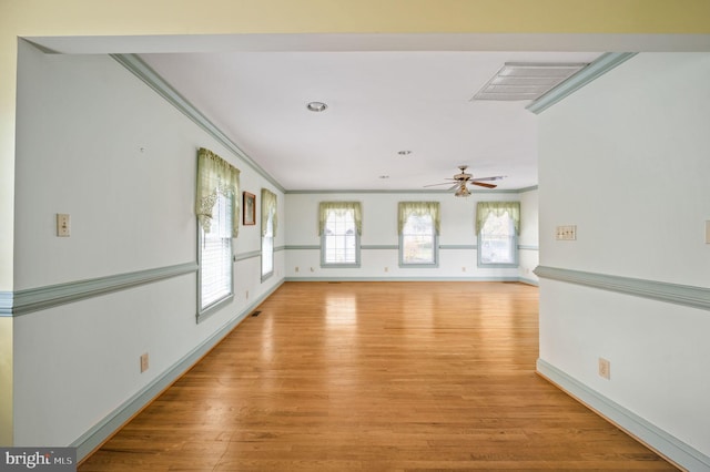 empty room featuring a ceiling fan, light wood-style floors, baseboards, ornamental molding, and visible vents