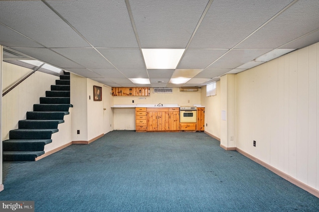finished basement featuring dark colored carpet, baseboards, stairs, and a paneled ceiling