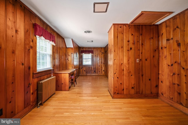 corridor with light wood-type flooring, visible vents, wood walls, and radiator