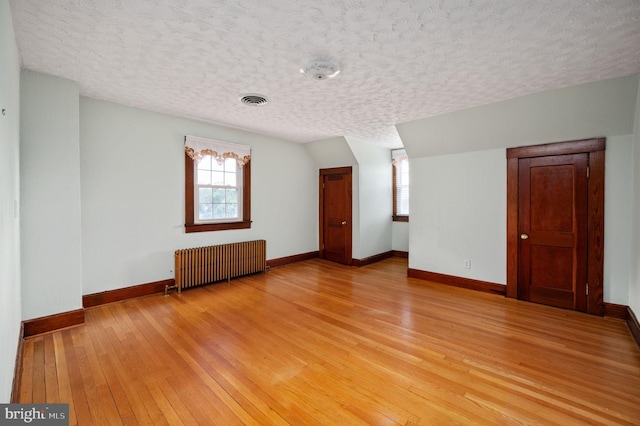 interior space featuring baseboards, a wealth of natural light, radiator heating unit, and light wood-style flooring