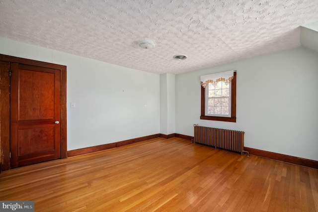 unfurnished room featuring light wood finished floors, a textured ceiling, radiator, baseboards, and visible vents