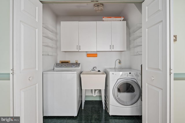 laundry area featuring washing machine and clothes dryer, cabinet space, a sink, and dark tile patterned flooring