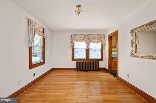 unfurnished room with radiator heating unit, light wood-style flooring, and baseboards